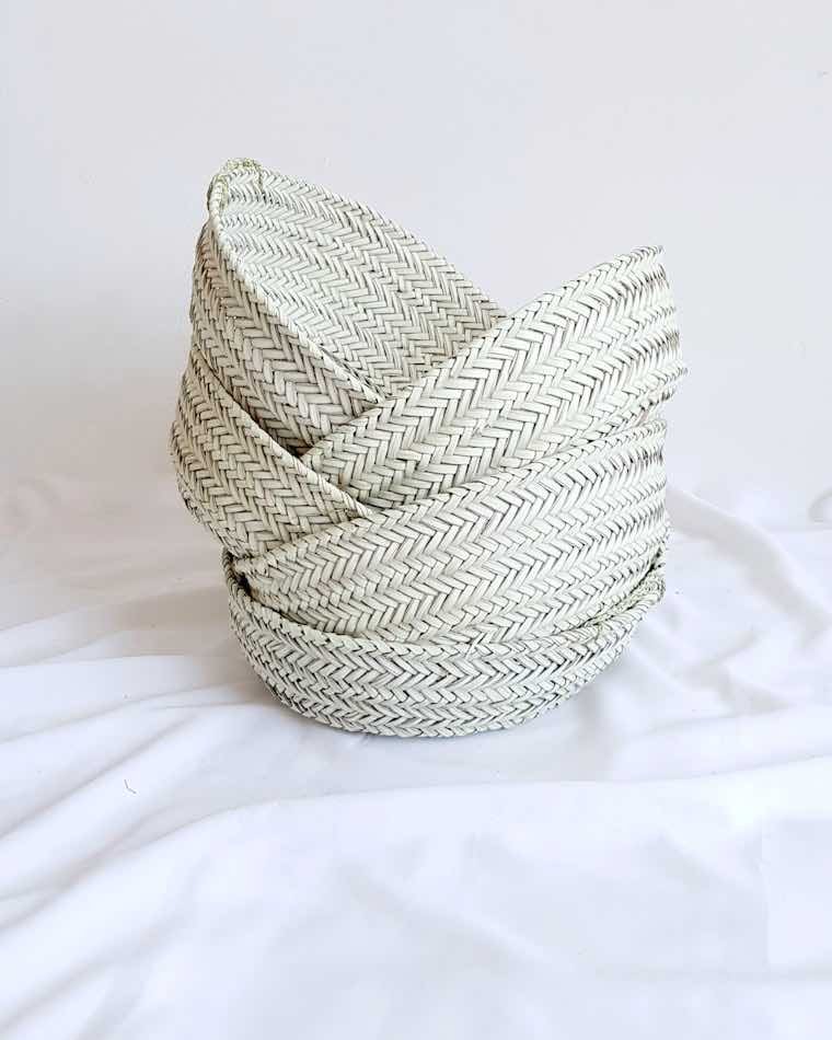 Canasto redondo tejido en fibra natural sobre un textil blanco