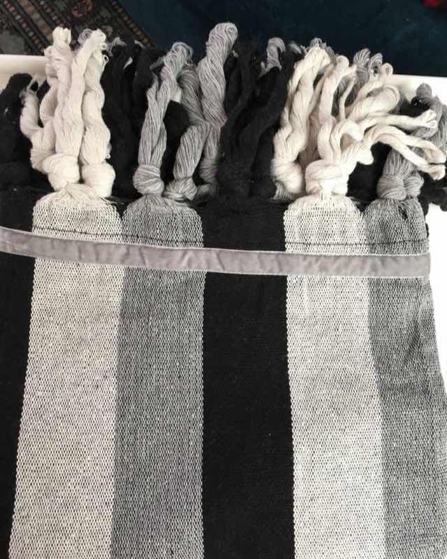 Jerga decorativa de lana con franjas grises y negras rematada con borlas