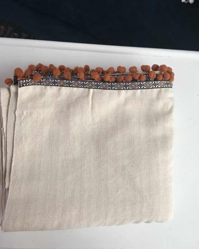Manta de algodón crudo rematada con pompones color terracota y cinta bordada