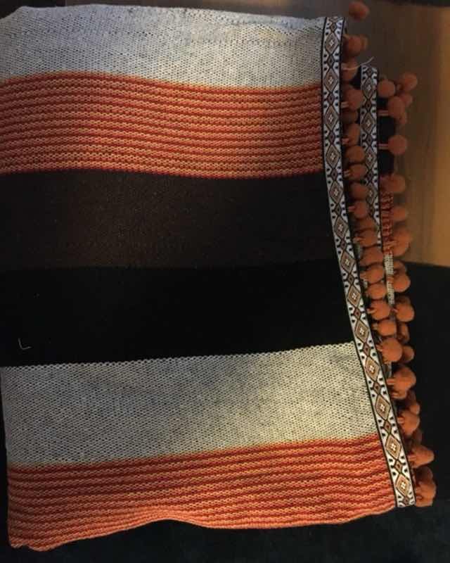 Manta tejida a mano con franjas terracota, negro y gris rematada con pompones