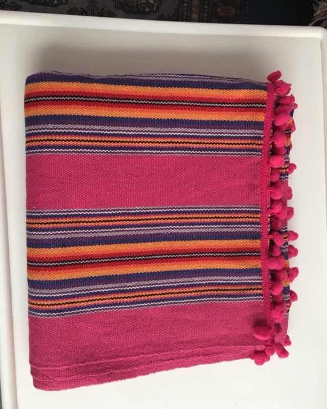 Manta de rayas fucsia, naranja y morado rematada con pompones rosados