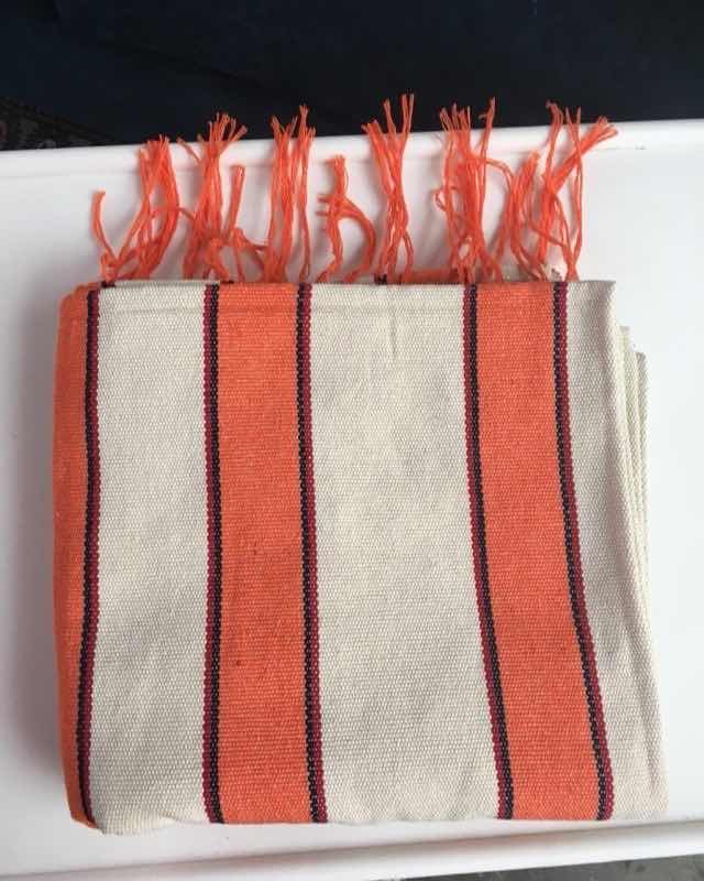 Toalla de picnic tejida a mano con rayas naranja sobre fondo crudo y flecos