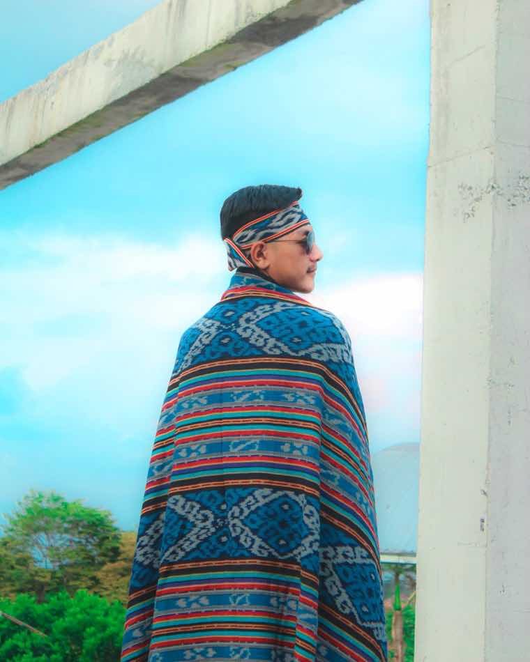 Persona abrigada con un poncho andino de colores junto a una ventana